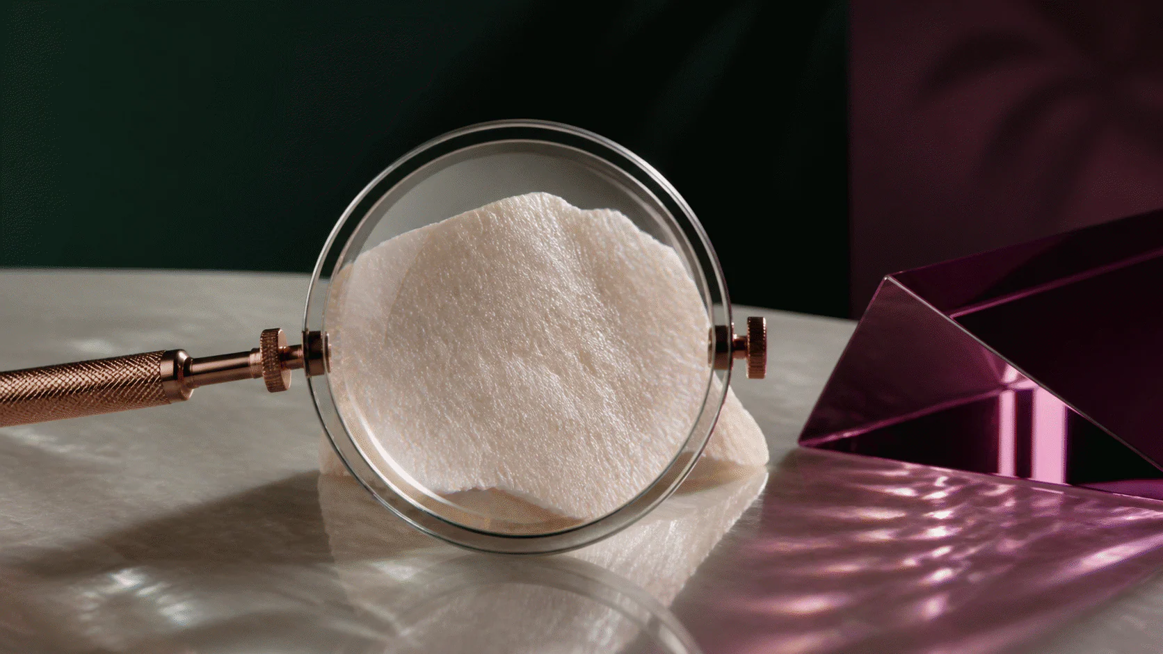 Clear magnifying lens examining a textured pearlescent material beside a reflective plum glass prism.