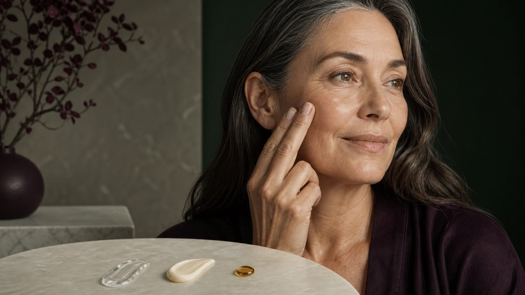Mature woman pressing fingertips to her cheek beside separate water-gel, cream, and facial-oil textures.