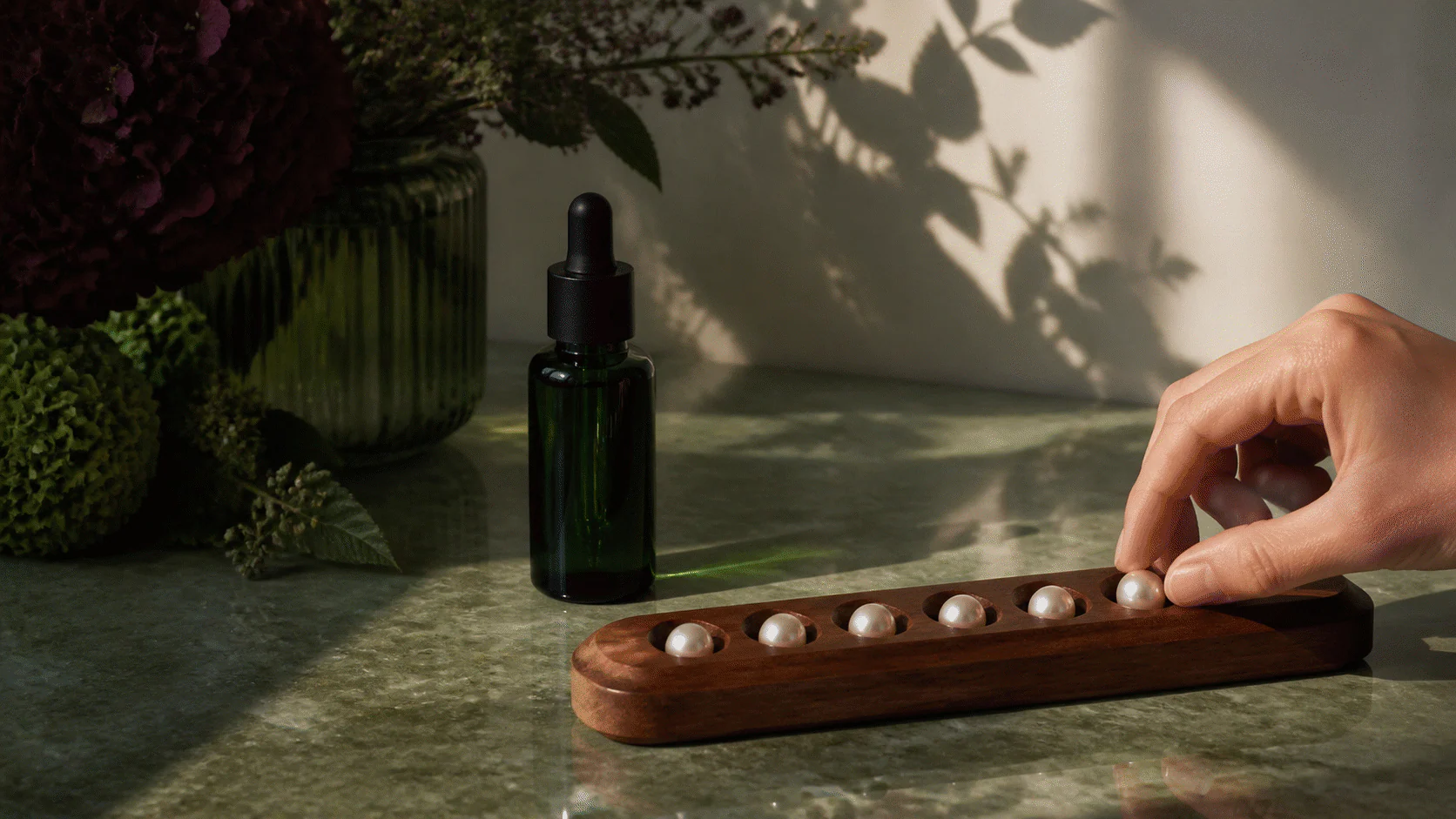Dark-green serum bottle beside a hand moving a pearl on an unmarked seven-bead wooden tracker.