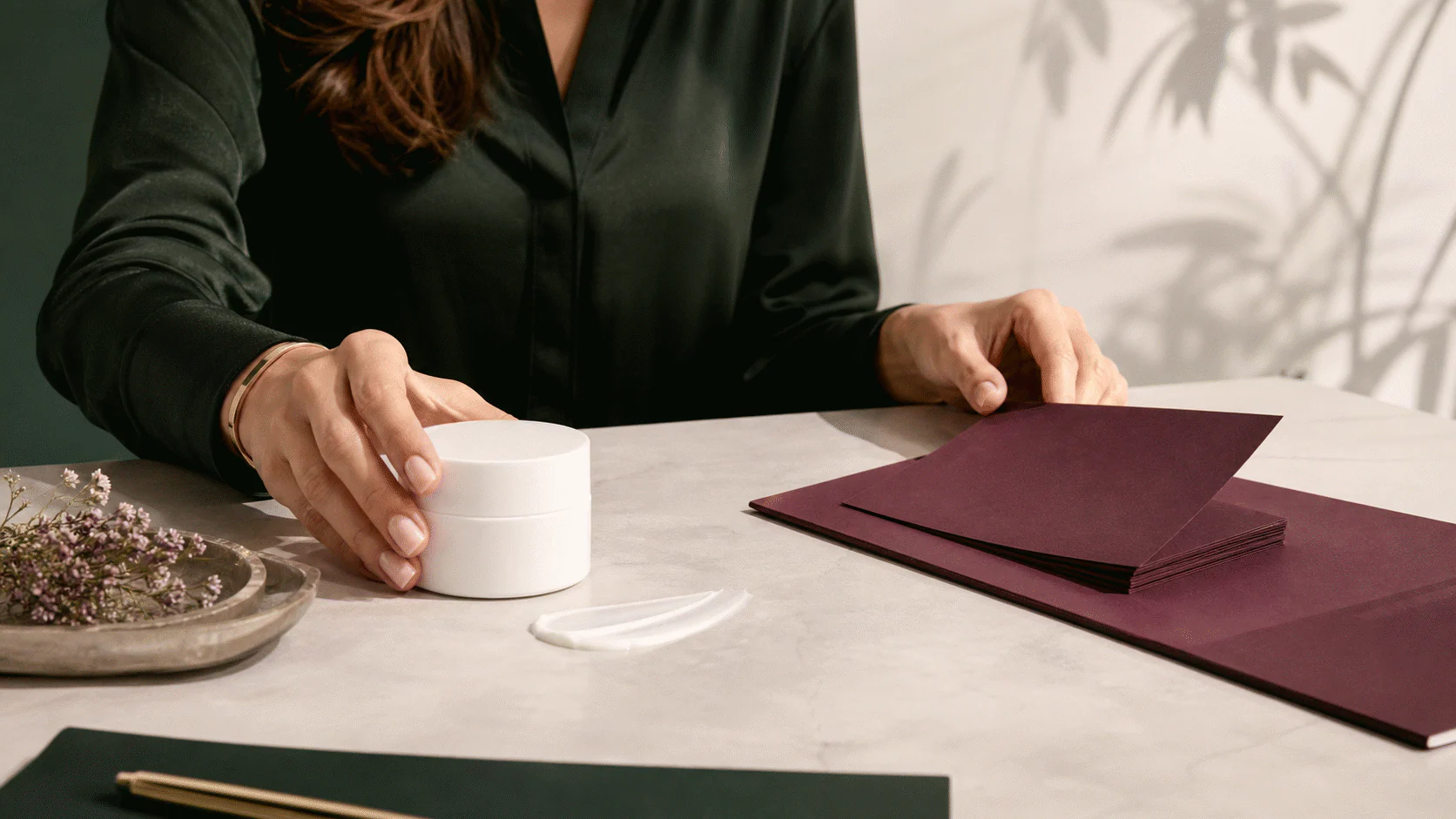 Reviewer separating a plain cream jar from a stack of blank plum promotional cards on a stone desk.