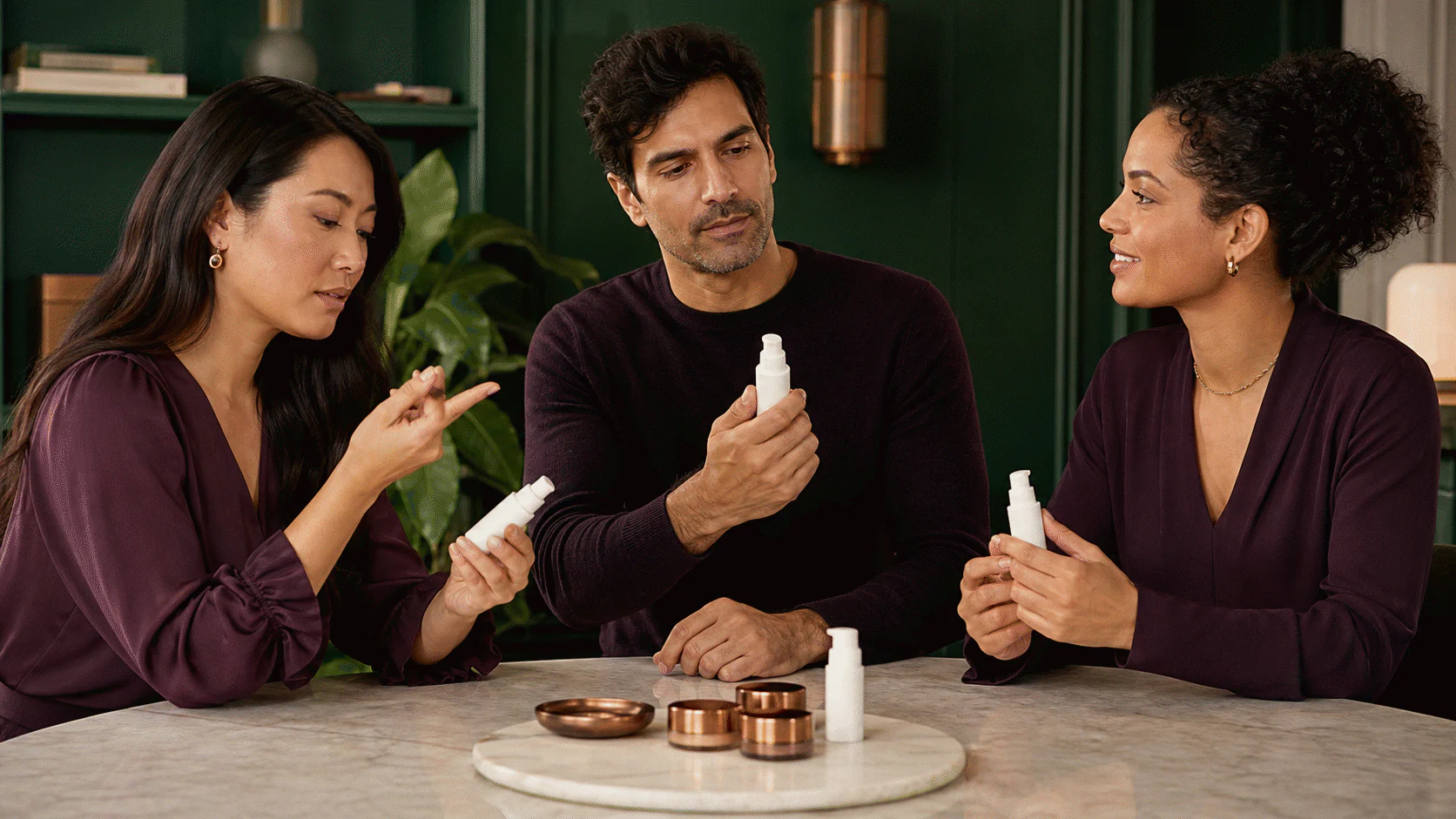 Three diverse adults evaluating identical small unlabelled pumps together in a refined green room.